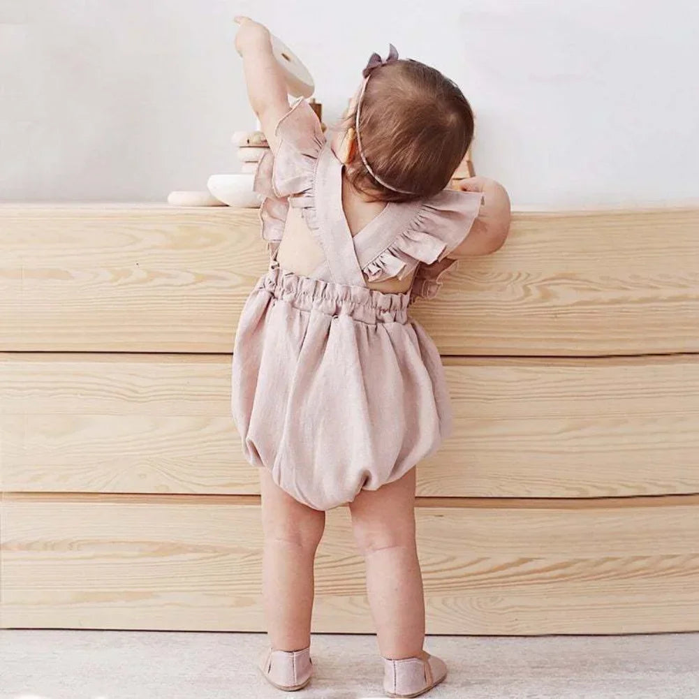 Shop BabyLove Ruffled Romper at BubeBaby, perfect for baby girls aged 0-24 months. Made from soft cotton, this sleeveless romper features a ruffled design and a covered button closure. Available in sizes for 3-24 months, it fits true to size and is ideal for summer